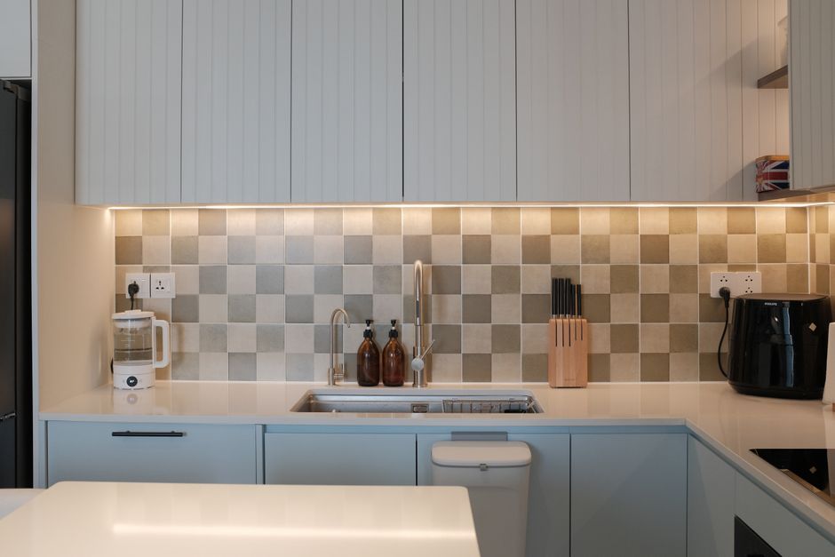 Cozinha moderna com armários brancos, bancada de quartzo, backsplash de azulejos em tons neutros e eletrodomésticos essenciais.