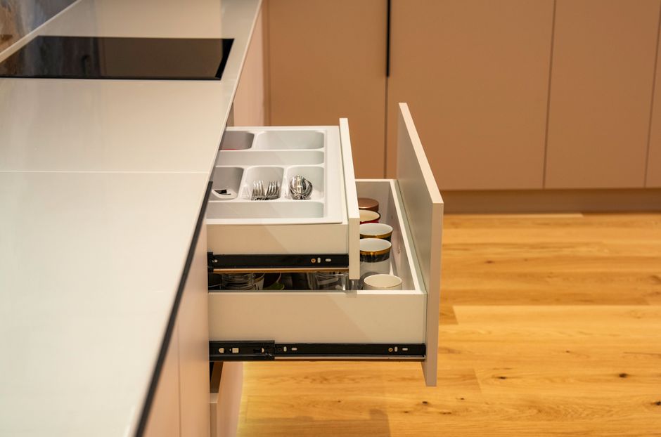 Canto de uma cozinha moderna com gaveta de utensílios e organização de xícaras e talheres.