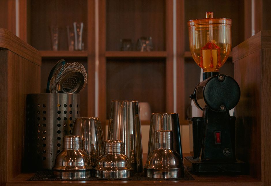 Imagem de uma estação de preparo de drinks com utensílios e uma máquina de liquidificador em um ambiente aconchegante de bar.