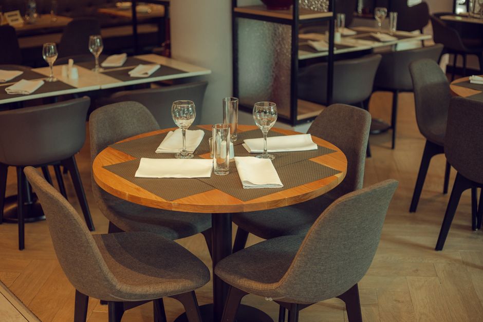 Mesa de restaurante preparada para receber hóspedes com taças de água, pratos e talheres, em ambiente elegante e acolhedor.