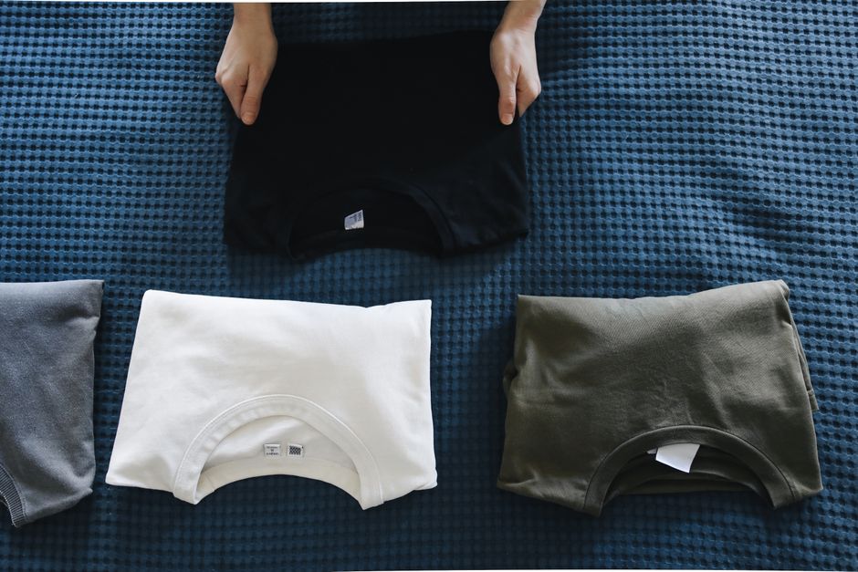 Homem organizando camisetas dobradas em uma cama, mostrando rotina de preparação e arrumação.