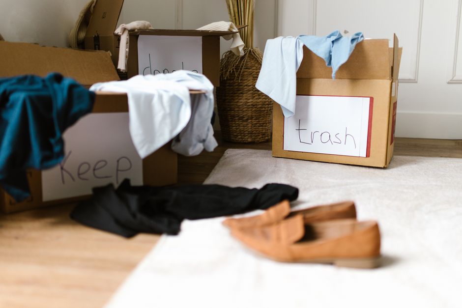 Imagem de caixas de mudança e roupas espalhadas, simbolizando organização e transplante de residência ou recomeço pessoal e profissional.