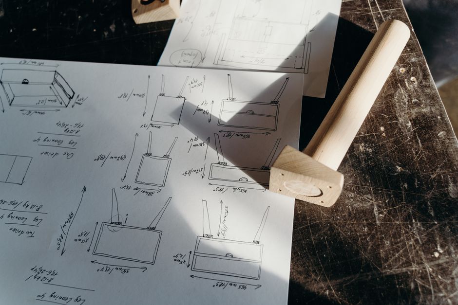 Imagem de um projeto técnico ou blueprint de um dispositivo ou estrutura, com desenhos e anotações em papel sobre uma mesa de trabalho.