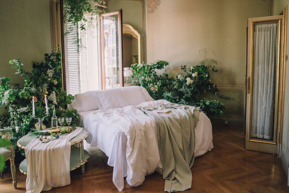 Salão de estar decorado de forma elegante com um sofá branco, janelas abertas, e plantas e flores que criam um ambiente acolhedor e sofisticado.