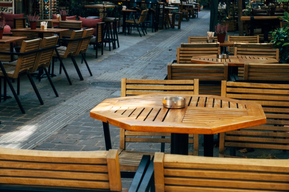 Imagem de uma área externa de restaurante com mesas de madeira vazias, ideal para ilustrar temas sobre gastronomia, lazer ao ar livre ou turismo.