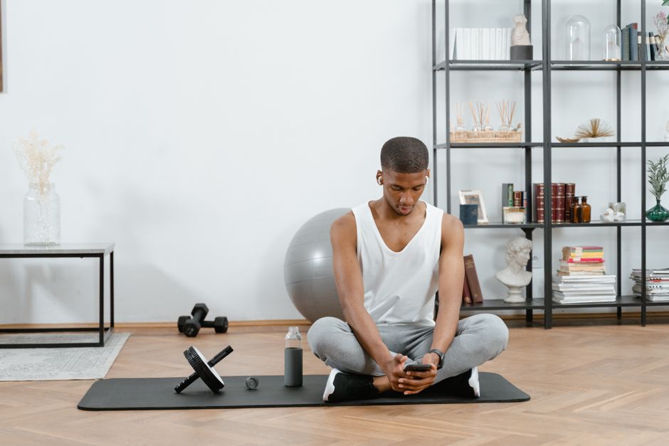 Homem praticando yoga ou meditação em um ambiente de sala de estar com elementos de decoração minimalista e roupas de prática física.