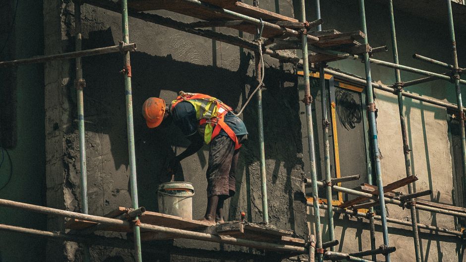 Profissional da construção civil trabalhando na fachada de um edifício em fase de reforma, utilizando equipamentos de segurança em um cenário de obras.