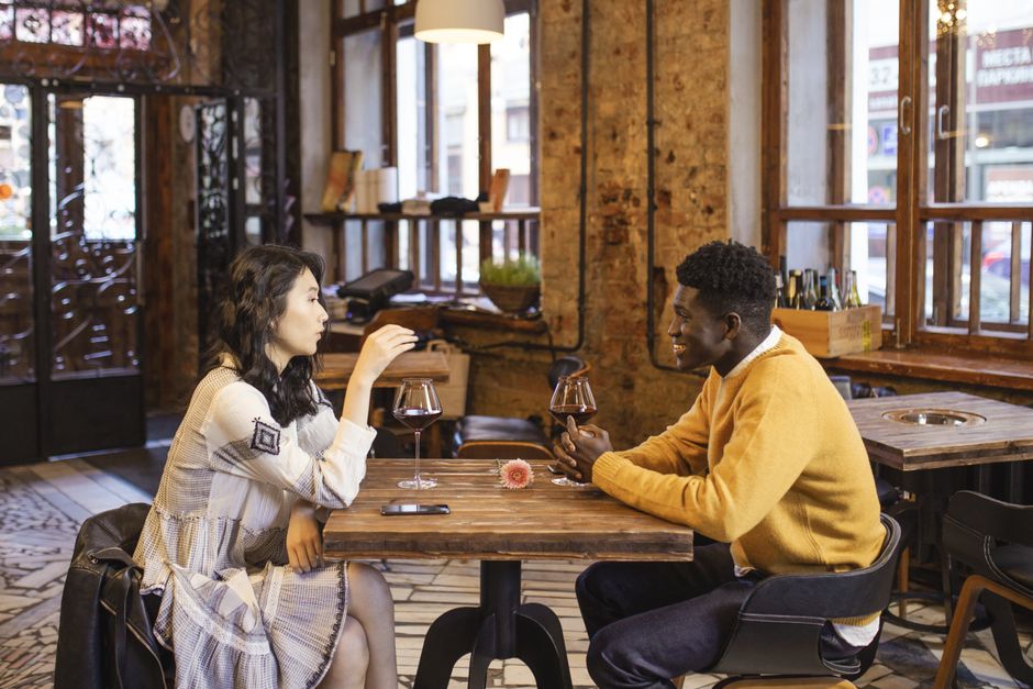 Dois jovens conversando e apreciando vinho em um ambiente acolhedor de café ou bar, criando uma atmosfera de socialização e lazer.
