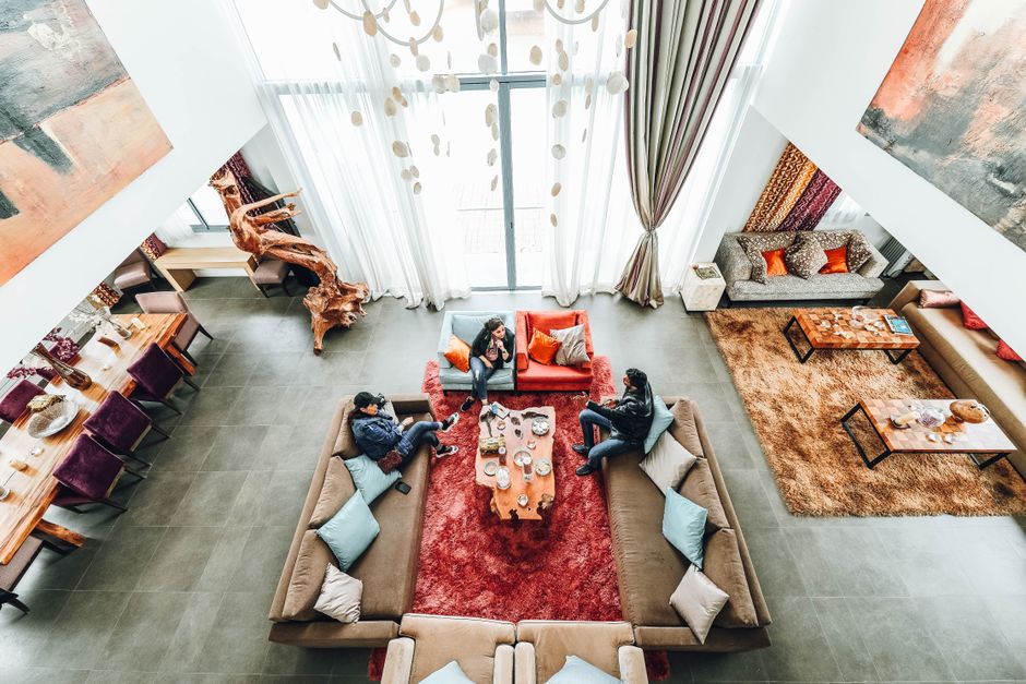 Imagem de uma sala de estar moderna com pessoas conversando e relaxando em um ambiente acolhedor e bem decorado.