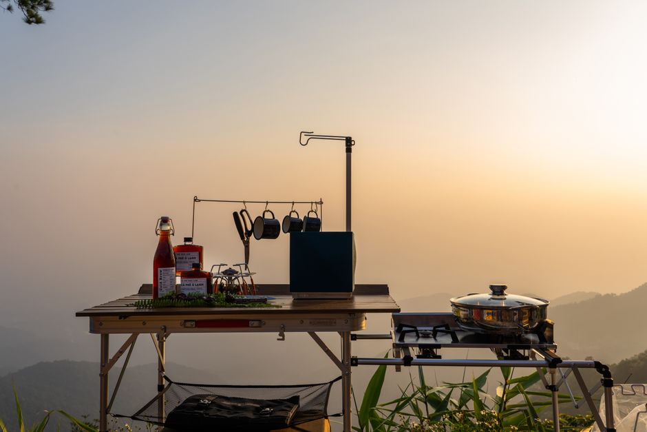 Imagem de uma cozinha ao ar livre ao entardecer com utensílios e ingredientes dispostos sobre uma mesa rústica, ideal para receitas ao ar livre ou churrascos em contato com a natureza.