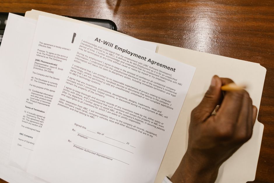 Pessoa assinando um contrato de emprego em uma mesa de madeira, simbolizando formalização de contratação.