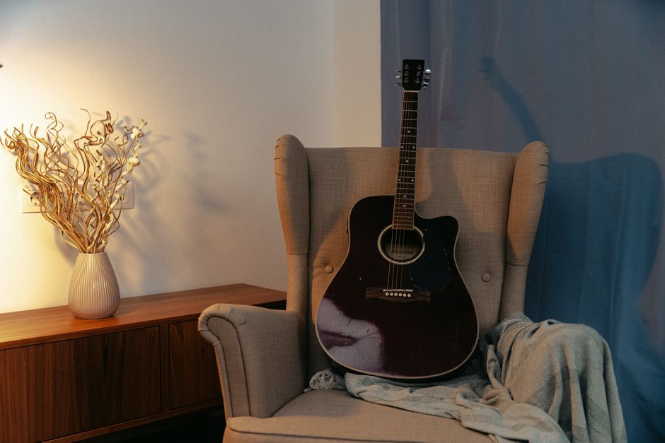 Imagem de uma sala aconchegante com um violão apoiado em uma poltrona confortável, ideal para ilustrar momentos de relaxamento ou criatividade musical.