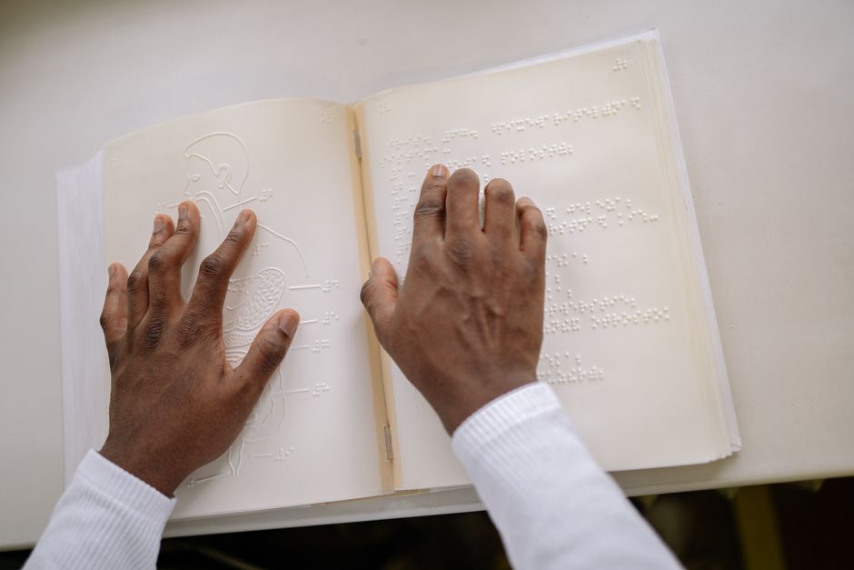 Pessoa lendo um livro em braile, destacando a inclusão e acessibilidade na leitura e na educação.