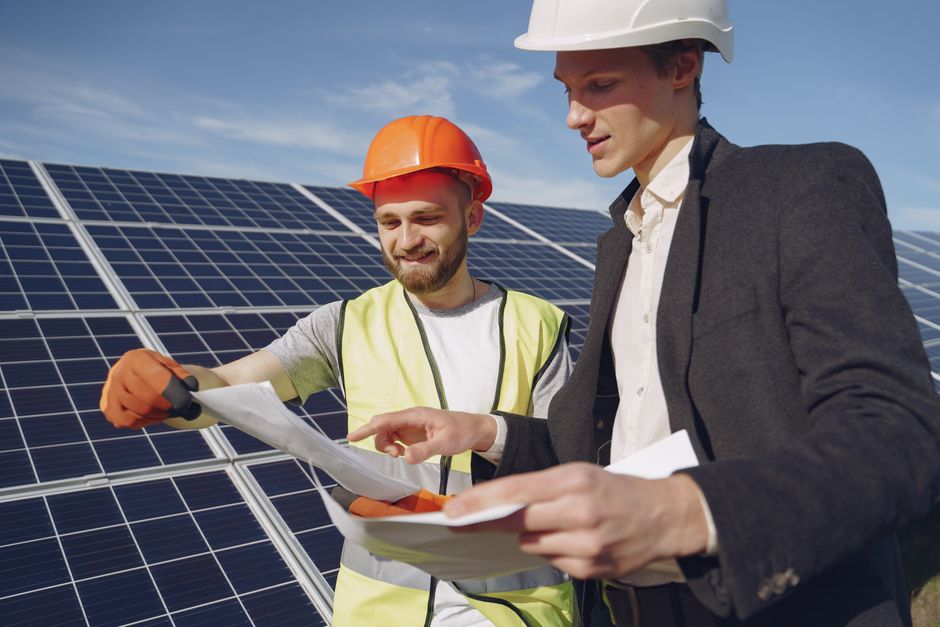 Engenheiros inspecionando painéis solares em uma usina de energia solar ao ar livre.