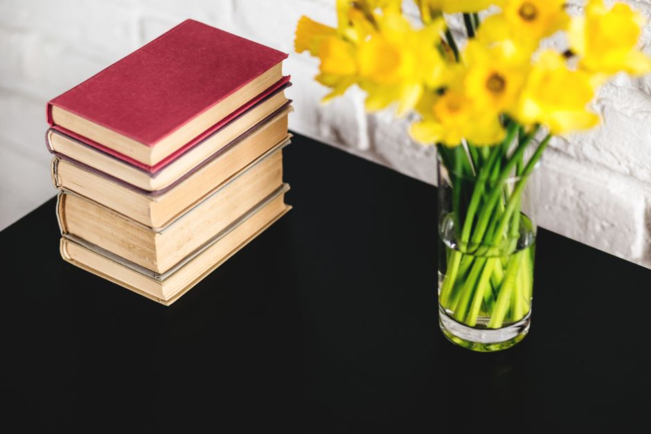 Reunião de livros clássicos ao lado de um vaso com flores amarelas, representando cultura e estética em um ambiente de estudos ou leitura.