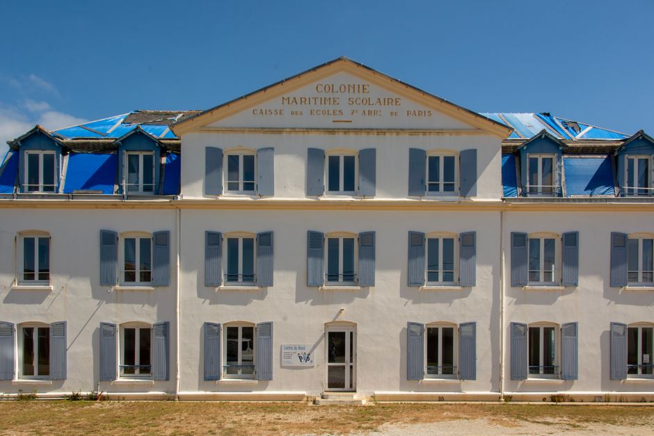 Imagem de um prédio antigo com fachada branca e janelas com persianas azuis, simbolizando história e arquitetura clássica de uma colônia marítima escolar, ideal para artigos sobre educação internacional ou história colonial.