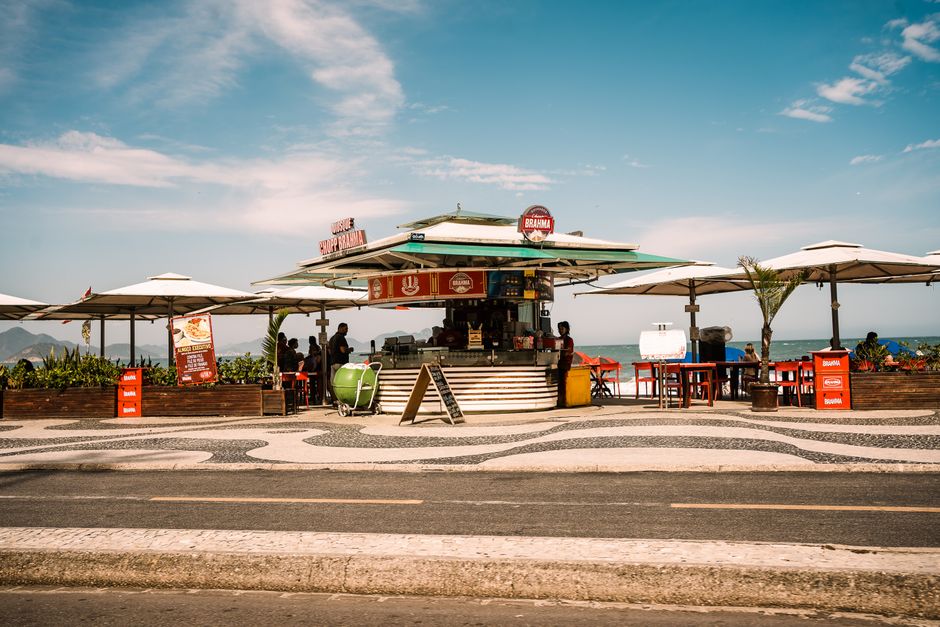 Imagem de uma barraca de comida de rua em um ambiente ao ar livre com vista para o mar, ideal para artigos sobre lazer, turismo ou gastronomia na praia.