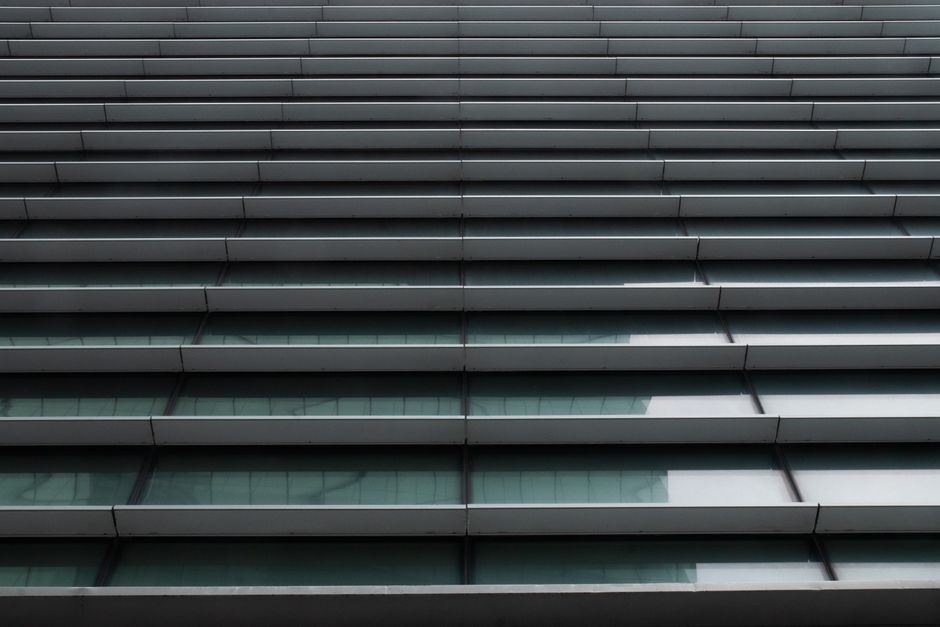 Imagem de uma fachada de edifício moderno com janelas de vidro e persianas fechadas, transmitindo uma sensação de arquitetura contemporânea e urbanismo.