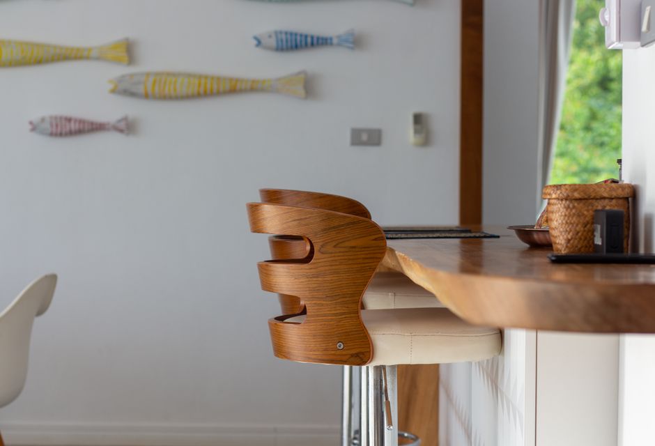 Cadeira infantil de design moderno ao lado de uma bancada de madeira em uma cozinha com decoração minimalista e detalhes coloridos nas paredes.