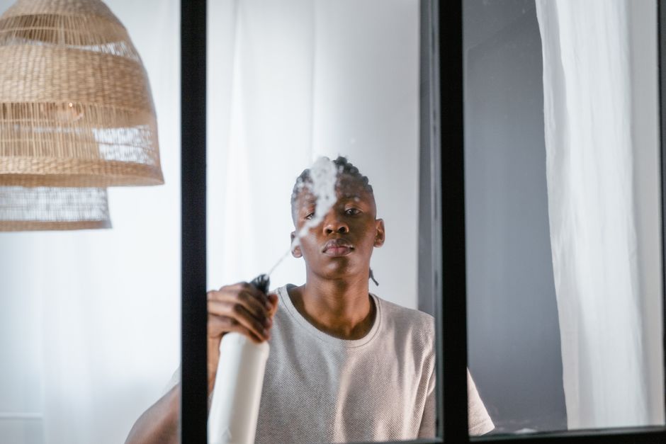 Pessoa usando spray de cabelo diante de um espelho, focando na rotina de cuidados pessoais em um ambiente doméstico.