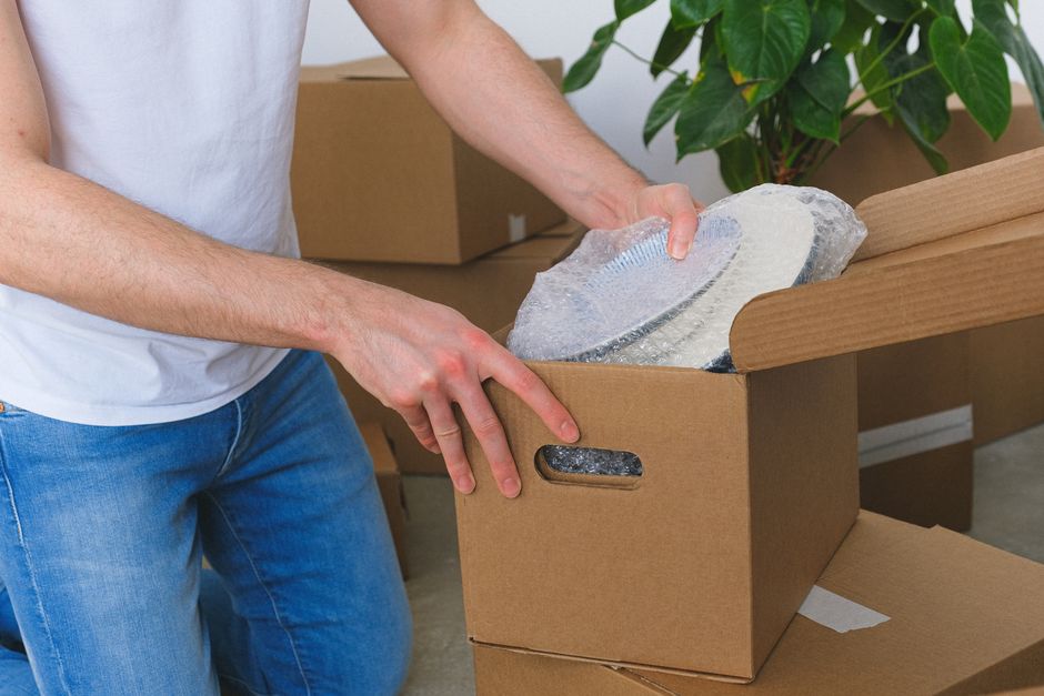 Pessoa desempacotando um item em uma caixa de papelão, indicando mudança ou organização residencial ou empresarial.