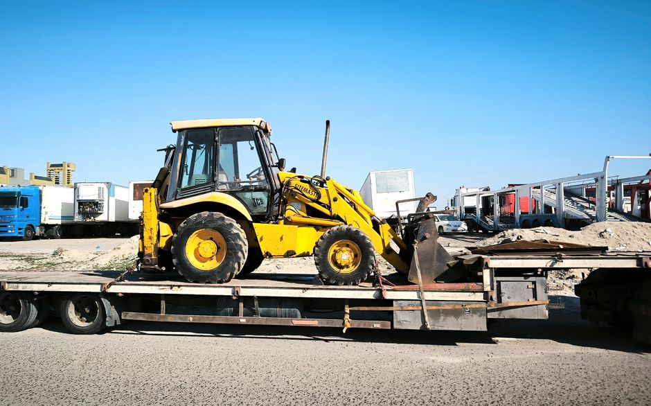 Imagem de um trator amarelo carregado em um caminhão, sugerindo transporte de maquinário pesado para obras ou construção civil.
