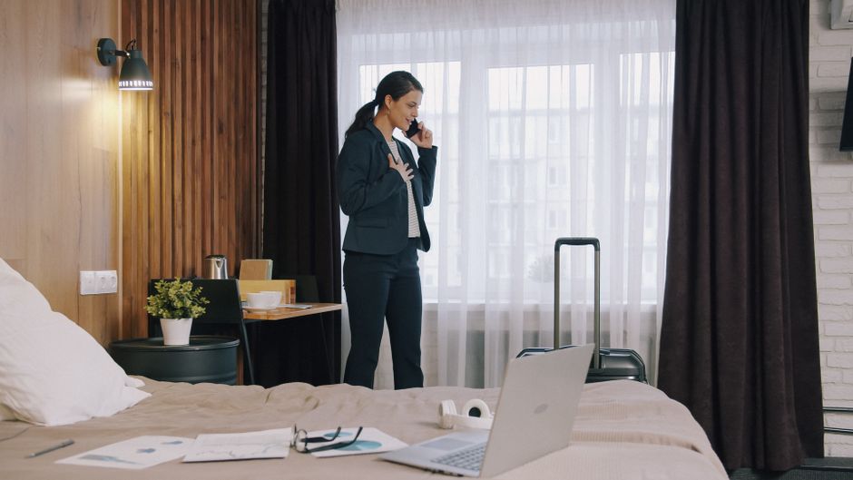 Mulher de negócios falando ao telefone enquanto organiza uma viagem de negócios em um hotel, refletindo planejamento e preparação para compromissos profissionais.