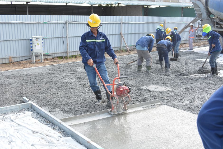 Equipe de trabalhadores em uma obra de pavimentação com concretagem do chão, destacando o trabalho em equipe na construção civil.