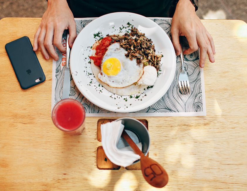 Imagem de uma pessoa apreciando uma refeição com ovos, arroz e molho de tomate, vista de cima em um ambiente de café da manhã ou brunch.