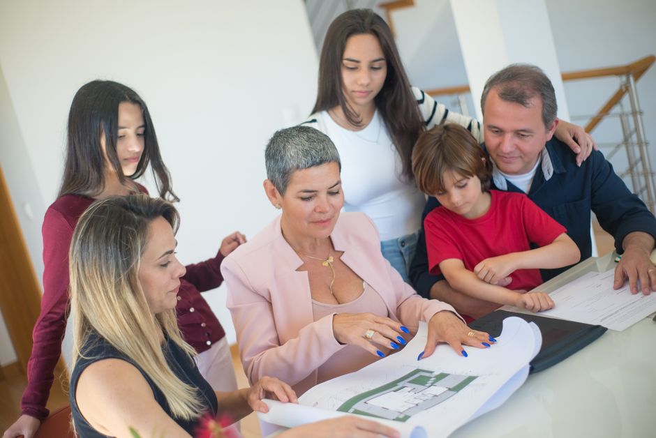 Família analisando planos de residência com profissional em uma reunião de planejamento.