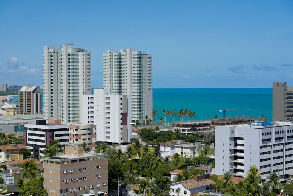 Imagem de um bairro com edifícios altos e vista para o mar, transmitindo uma atmosfera urbana e litorânea.