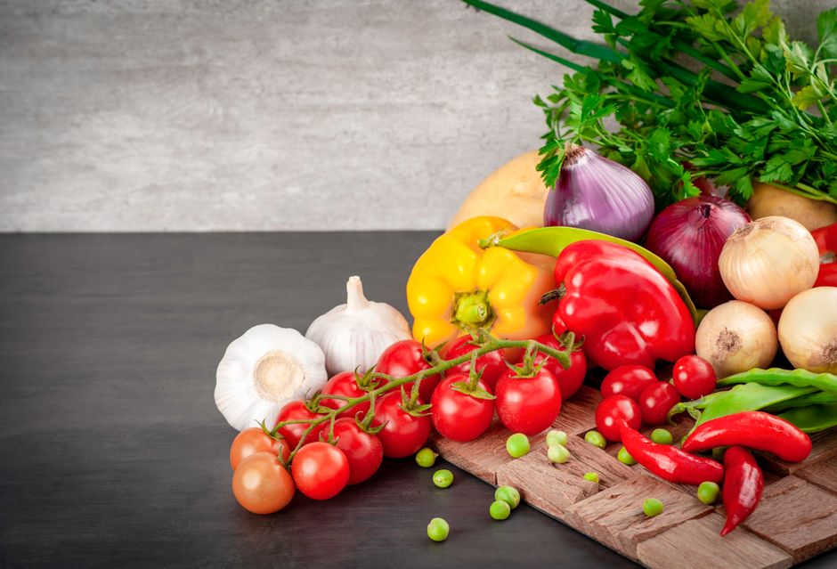 Imagem de ingredientes coloridos e variados de hortifrúti dispostos sobre uma mesa de madeira, enfatizando alimentos naturais e saudáveis.