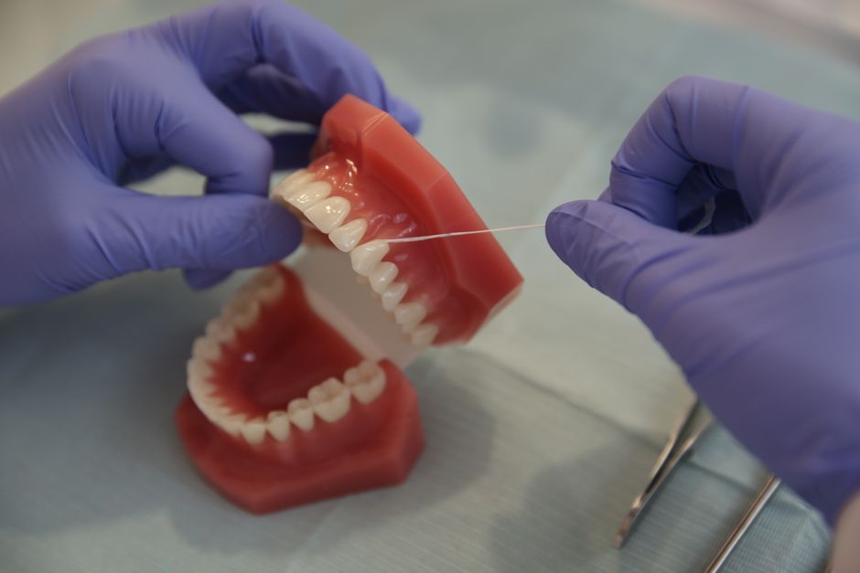 Mãos usando luvas estão limpando ou ajustando um modelo de prótese dentária com uma linha de precisão, em um ambiente odontológico.