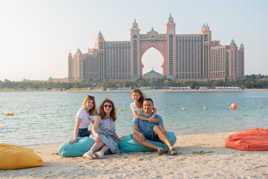 Família relaxando na praia com um hotel luxuoso ao fundo, ideal para artigos sobre turismo familiar e destinos de viagem de alto padrão.
