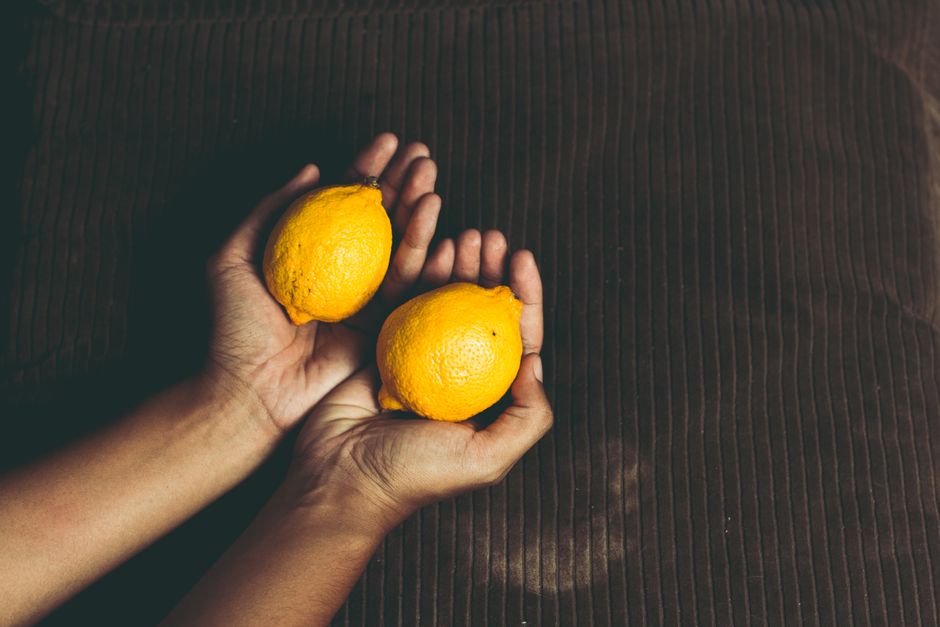 Mãos segurando dois limões amarelos sobre uma superfície escura, destacando o tema de alimentos naturais e frescos.