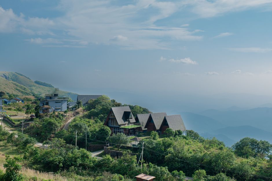 Paisagem de casas em encosta de montanha com vista para o céu e nuvens, ilustrando tranquilidade e conexão com a natureza.
