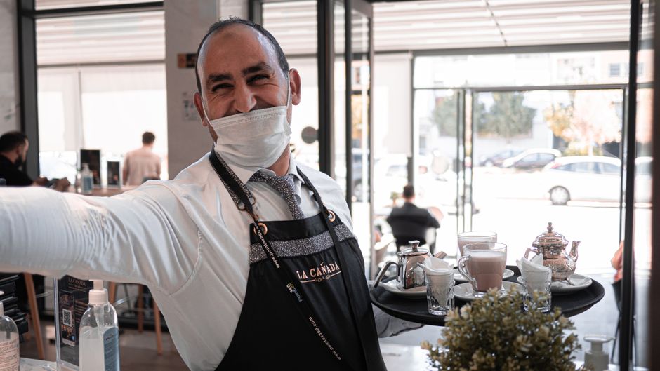 Barista sorridente oferecendo uma bandeja com bebidas em um café moderno e acolhedor.