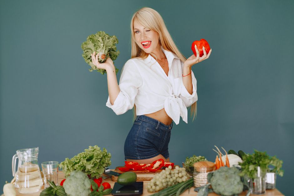 Mulher feliz segurando ingredientes frescos de hortifrúti em uma cozinha, destacando alimentação saudável e estilo de vida saudável.