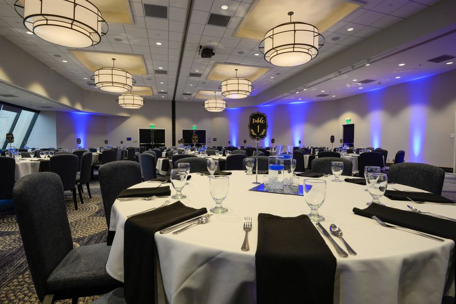 Ambiente elegante de evento corporativo ou celebração, preparado com mesas decoradas e iluminação sofisticada.