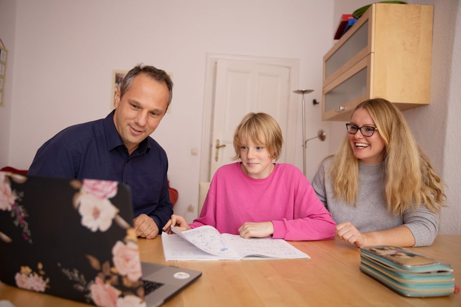 Família estudando e interagindo com conteúdo digital e papel em um ambiente doméstico, promovendo aprendizado e lazer em conjunto.