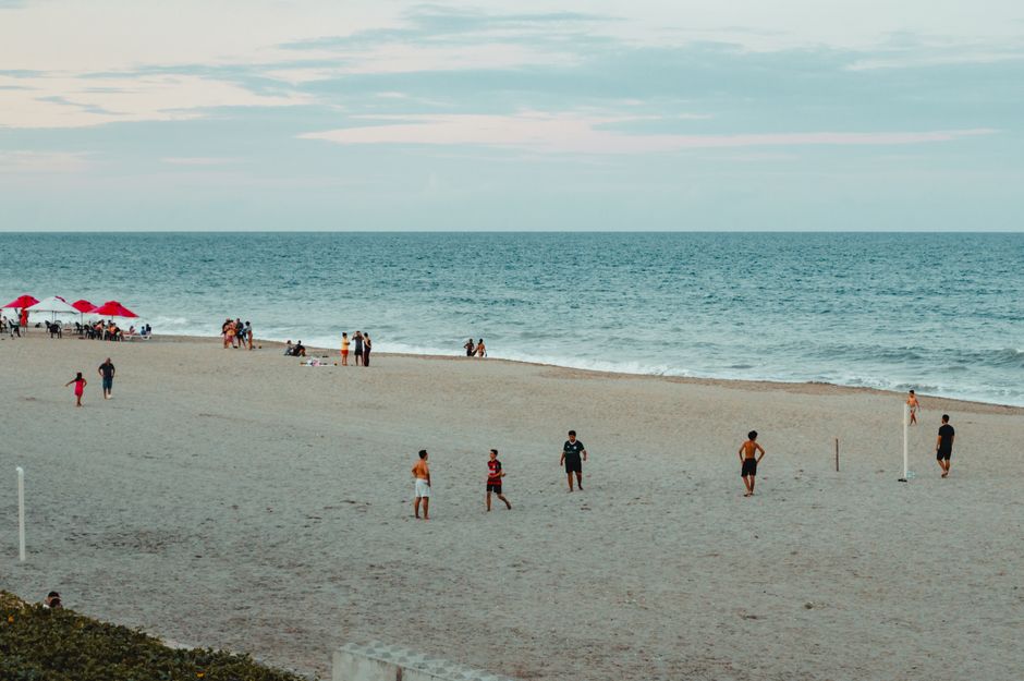 Praia com pessoas aproveitando o mar e a areia em um dia ensolarado, ideal para artigos sobre lazer ou turismo à beira-mar.