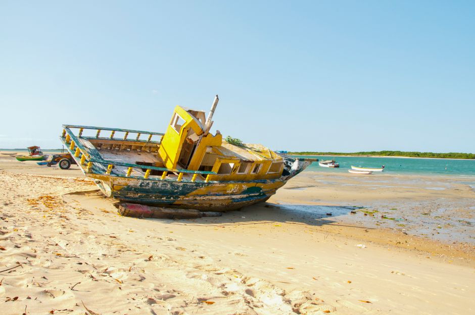 Barco abandonado na praia, simbolizando abandono ou momentos de transição na vida marítima.