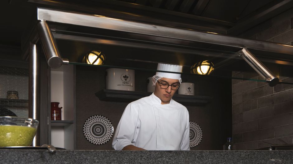 Chef de cozinha preparando prato em uma cozinha profissional, com foco na gastronomia e preparo de alimentos.