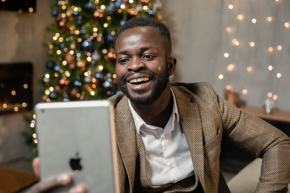 Homem sorridente em uma reunião virtual, com decoração de Natal ao fundo, representando momentos de celebração e conexão profissional e pessoal no ambiente de trabalho.