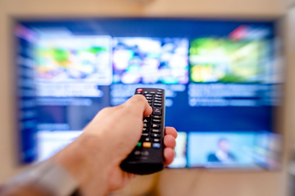 Pessoa assistindo a uma televisão com conteúdo de streaming usando controle remoto, destacando o consumo de mídia digital e entretenimento em casa.