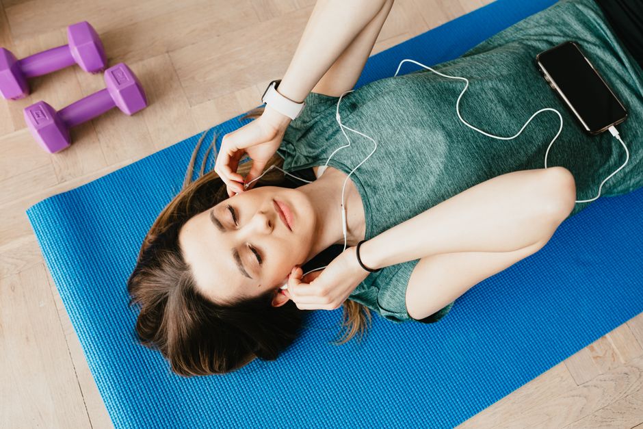 Mulher relaxando após treino, ouvindo música, em ambiente de home office ou academia.