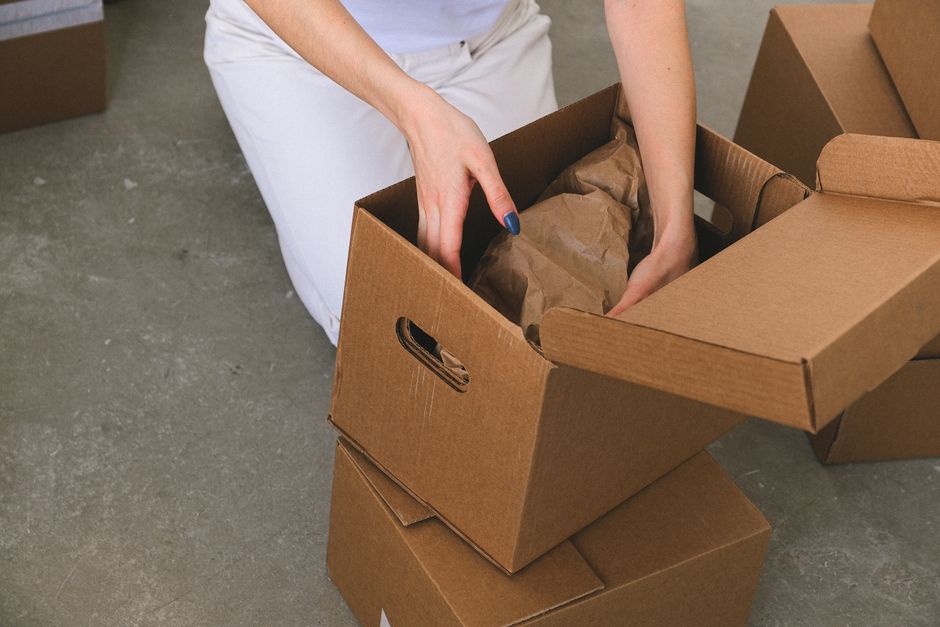 Pessoa organizando caixas de papelão em um ambiente de trabalho ou armazenamento, simbolizando gestão de inventário ou logística.