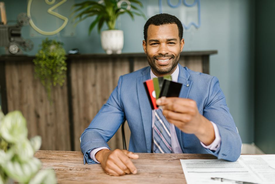 Homem de terno sorridente segurando cartões de crédito em ambiente de escritório, promovendo temas de finanças e gestão financeira.