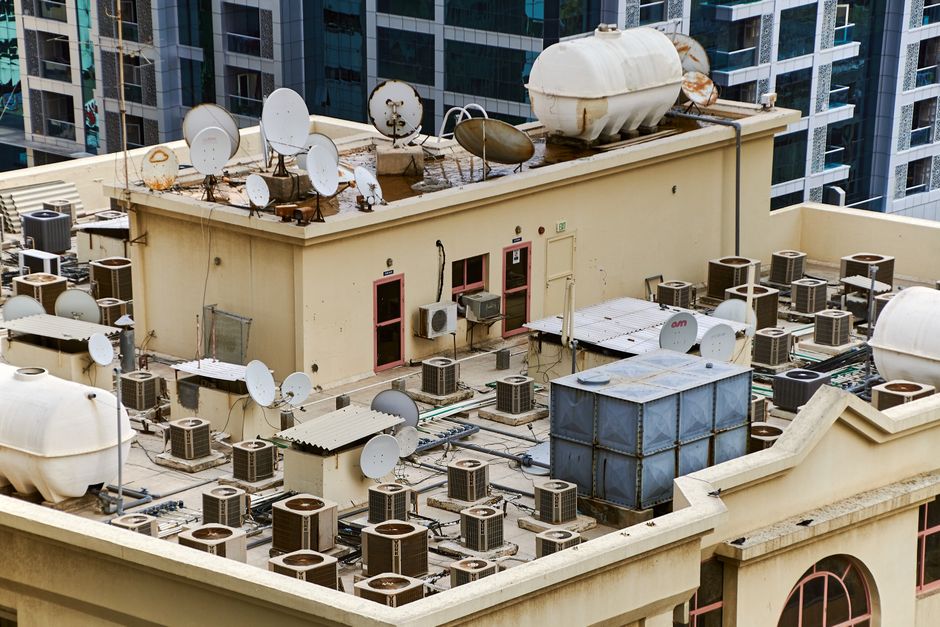 Imagem de um telhado de edifício com diversos satélites e sistemas de ar condicionado, evidenciando a infraestrutura tecnológica de um prédio corporativo.