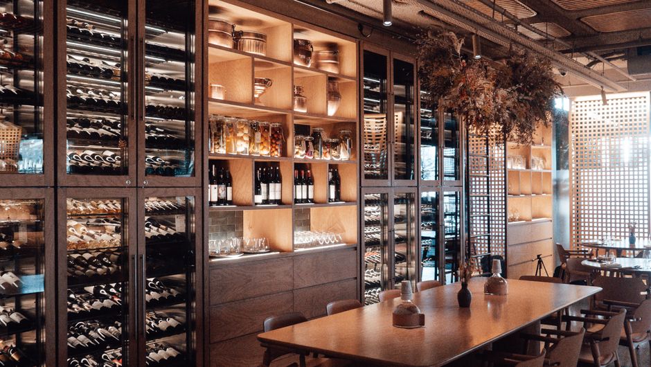 Ambiente de restaurante ou wine bar com prateleiras de vinhos, mesas e decoração aconchegante, ideal para artigos sobre experiências gastronômicas ou harmonização de vinhos.